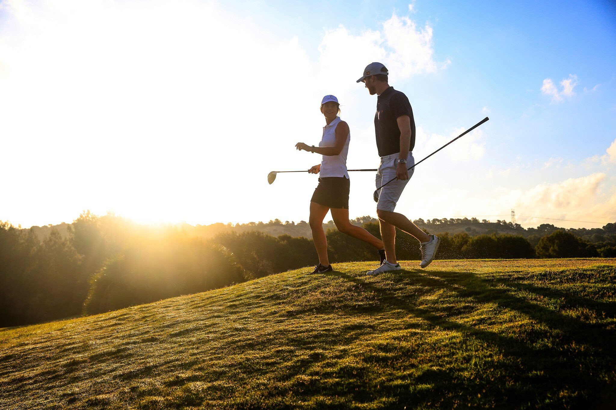 Golfspillere som har solnedgang bak seg